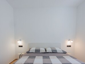 A bedroom with a bed, two wall-mounted lights, and a small table with a remote control. - Vacation home  by Interhome (Krneza)