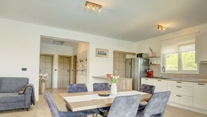 A modern kitchen with a dining area, featuring a wooden table, grey upholstered chairs, and a refrigerator. - Vacation home  by Interhome (Krneza)