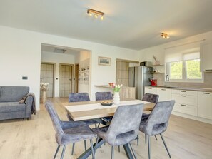 A modern kitchen with a dining area, featuring a wooden table, grey upholstered chairs, and a refrigerator. - Vacation home  by Interhome (Krneza)