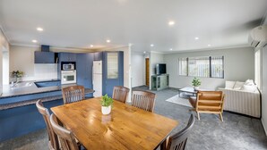Una cocina moderna con electrodomésticos integrados, un comedor con mesa y sillas de madera, y una sala de estar con sofá y televisor.