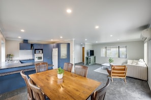 A modern kitchen with built-in appliances, a dining area with a wooden table and chairs, and a living room with a sofa and a TV.