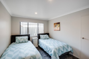 A bedroom with two beds, a window with blinds, a bedside table, and a door.