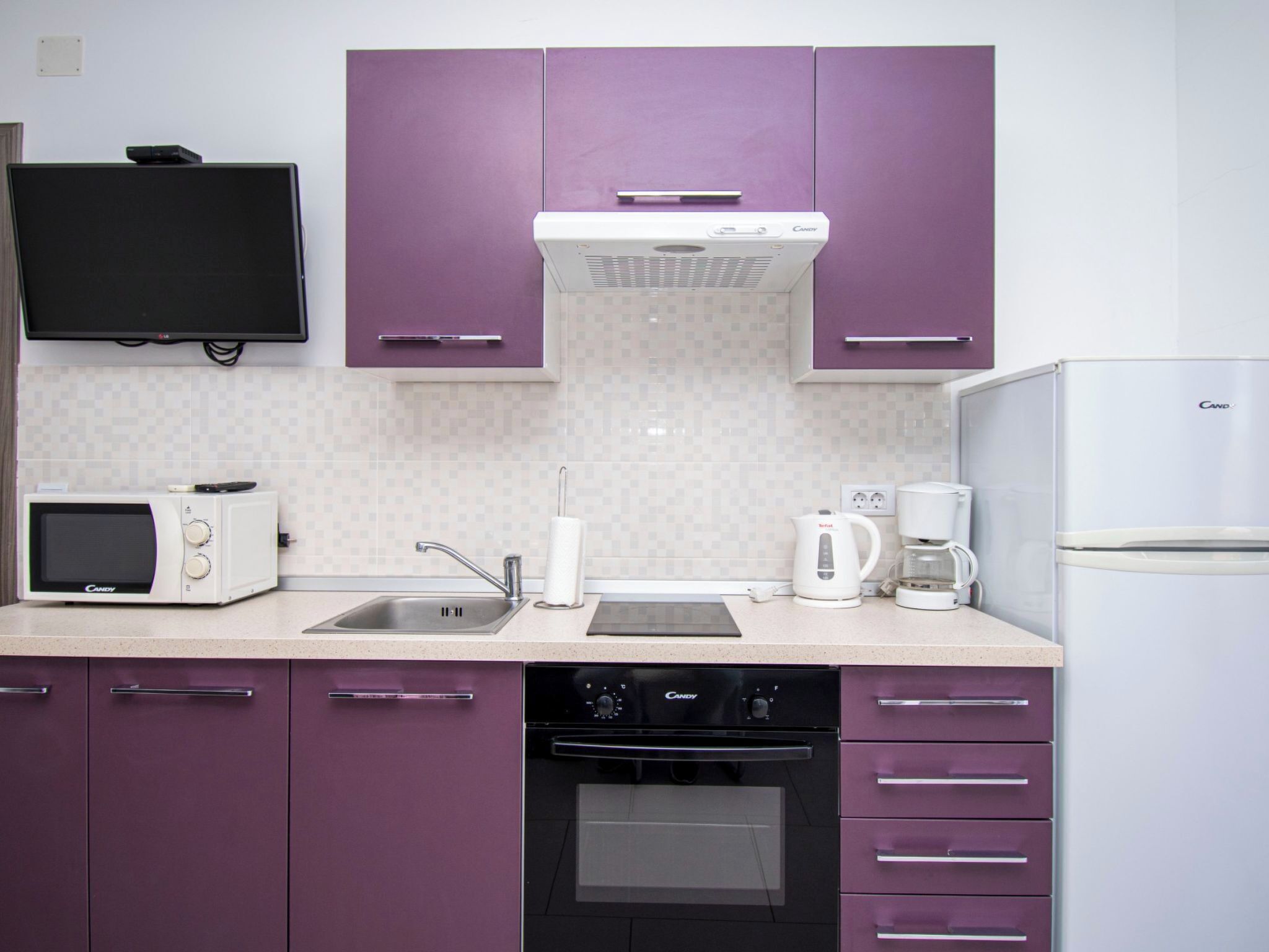 A kitchen with purple cabinets, a microwave, a toaster, a kettle, a coffee maker, a refrigerator, and a dishwasher.