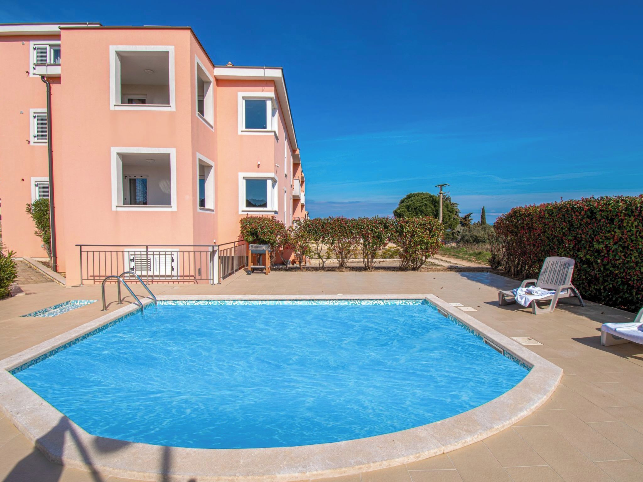 A swimming pool with a clear view of the sea, a building with balconies, and a sunny day.