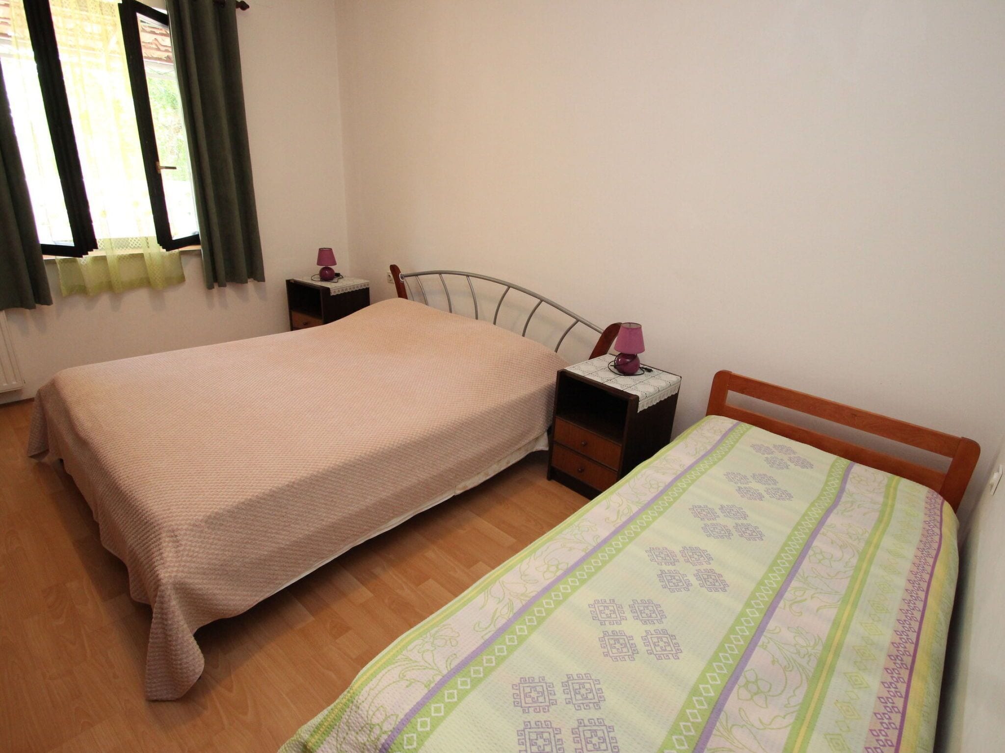 Una habitación con dos camas, una ventana con cortinas y una mesita de noche con lámpara.