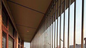 A corridor with a metal railing, large windows, and a view of greenery and buildings.
