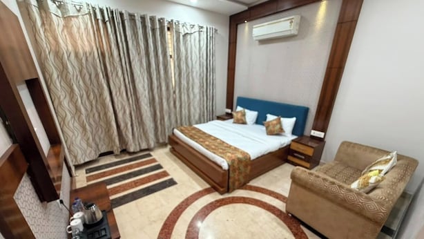 A hotel room with a bed, a sofa, a coffee table, a TV, and an air conditioning unit.