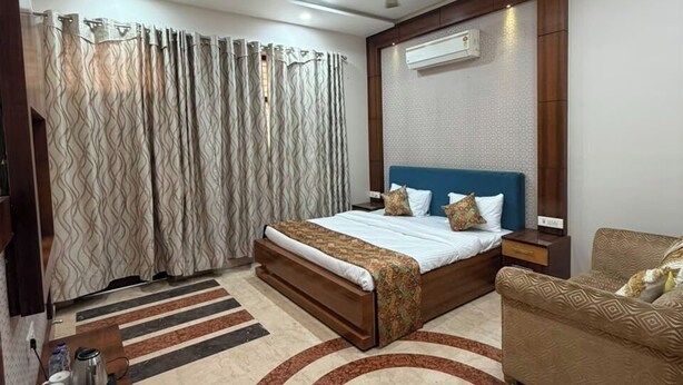 A hotel room with a bed, a sofa, a coffee table, a TV, and a bathroom area. - Rameshawram Sukoon Mansion (Varanasi)
