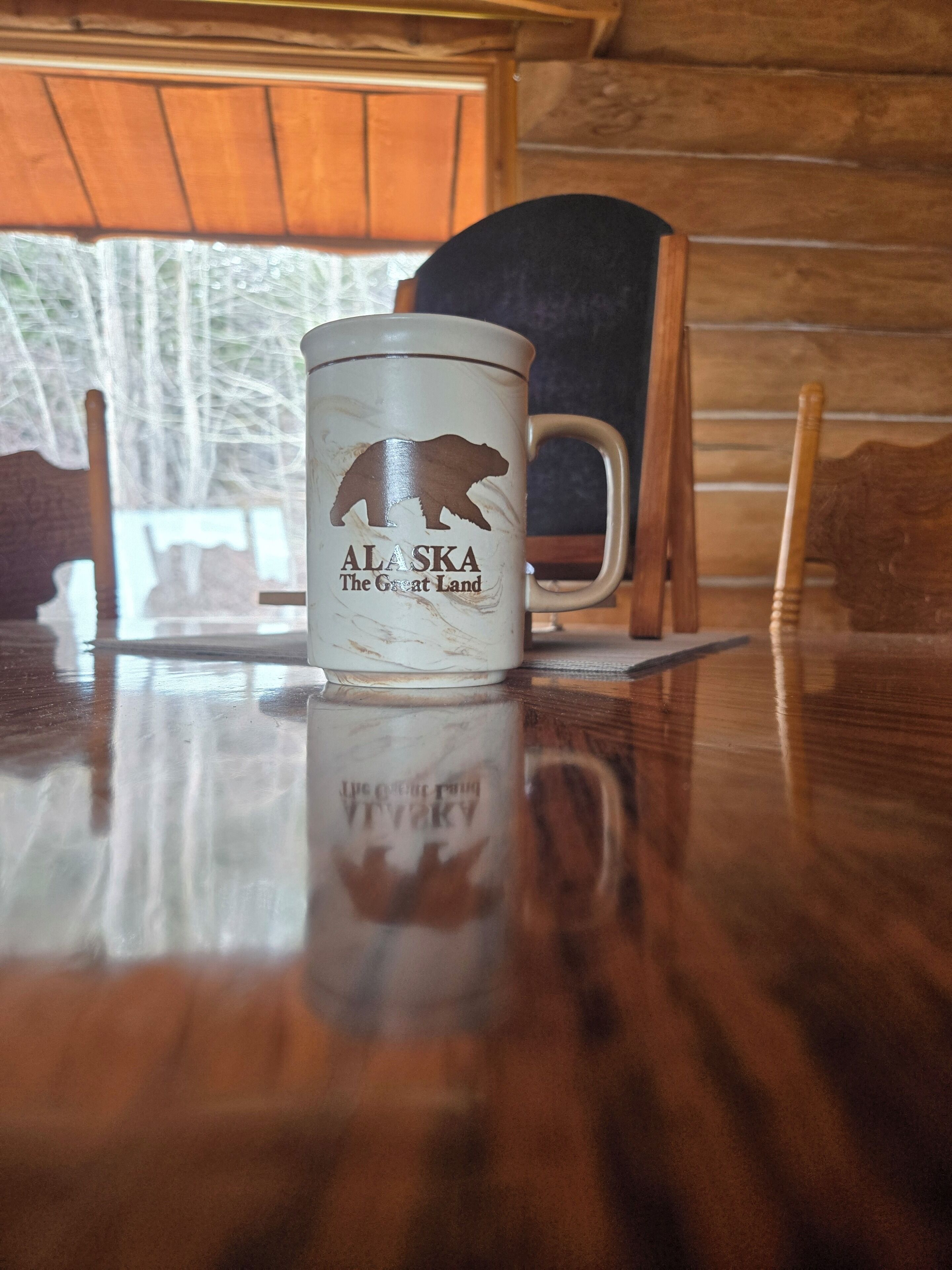 A wooden interior with a table displaying a mug featuring a bear and text 'Alaska The Great Land.'