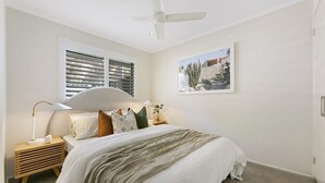 Ein Schlafzimmer mit Bett, Nachttischen, Deckenventilator und einem Fenster mit Jalousien.