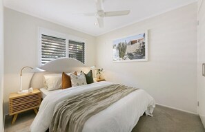 Ein Schlafzimmer mit Bett, Nachttischen, Deckenventilator und einem Fenster mit Jalousien.