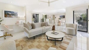 Ein modernes Wohnzimmer mit einer Couch, Sesseln, einem Couchtisch und einem Essbereich mit einem Glastisch.