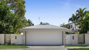 Ein eingeschossiges Haus mit Garage, umgeben von einer Steinmauer und Palmen.