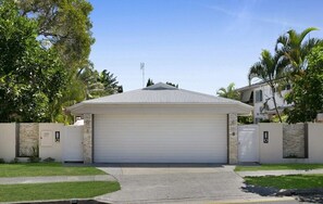 Ein eingeschossiges Haus mit Garage, umgeben von einer Steinmauer und Palmen.