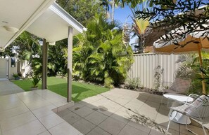Ein überdachter Patio-Bereich mit Sitzgelegenheit und einem gepflegten Garten.