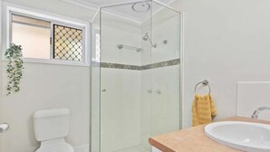 A bathroom with a glass-enclosed shower, a toilet, a sink, and a small window with a plant. - 2BR Paradise at Riviera (Gold Coast)