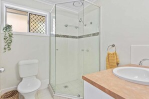 Ein Badezimmer mit einer Duschkabine, Toilette, Waschbecken und einem kleinen Fenster mit Pflanze.