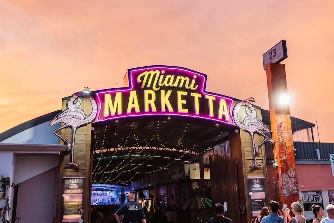 The entrance to Miami Market Place with a neon sign and a street number sign.