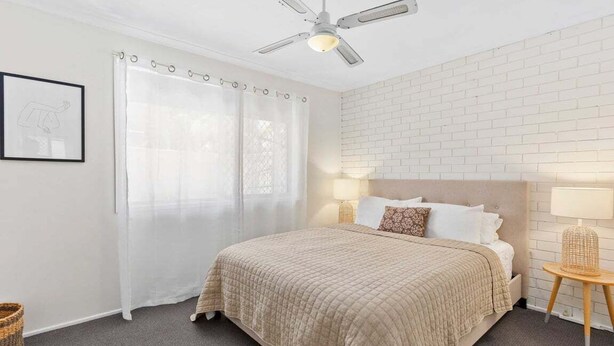A bedroom with a bed, a ceiling fan, a window with curtains, a wall-mounted lamp, and a framed picture. - 2BR Paradise at Riviera (Gold Coast)