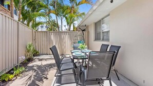 An outdoor patio with a table and chairs, surrounded by a wooden fence and palm trees. - 2BR Paradise at Riviera (Gold Coast)