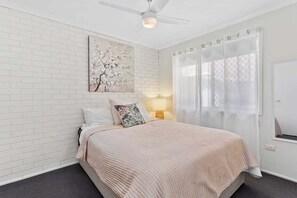 A bedroom with a bed, a ceiling fan, a window with a curtain, and a wall-mounted artwork. - Riviera Rd Miami - 2/29 (2B/1B) (Gold Coast)