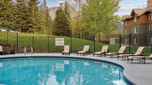 A swimming pool with lounge chairs, a lifeguard duty sign, and a mountainous backdrop. -  Spacious 2-bedroom condo in Magical Canmore with fitness room and AC (Canmore)