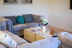 A living room with a grey sofa, a coffee table with a vase of flowers, and a painting on the wall.