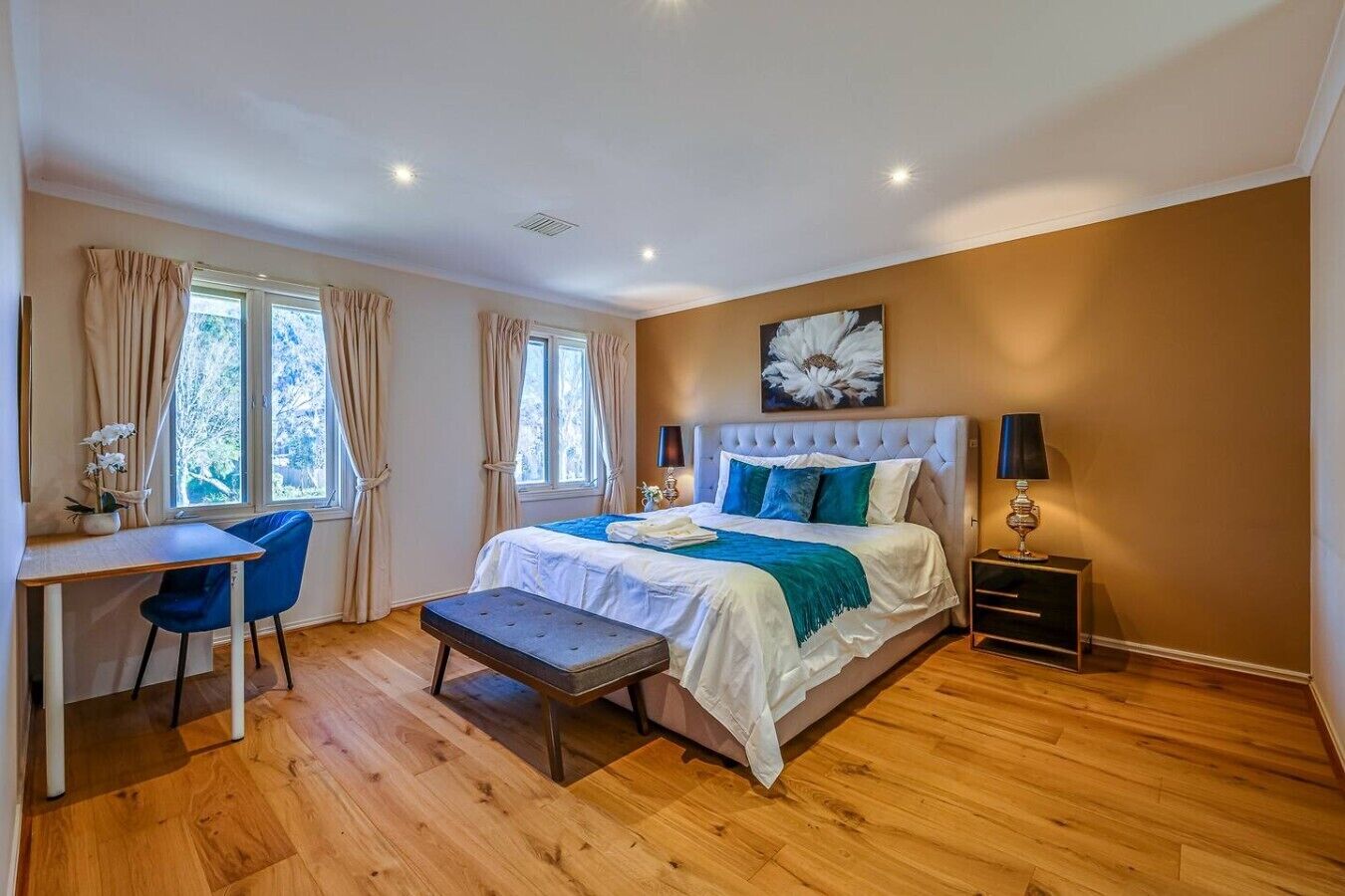 A bedroom with a bed, desk, chair, bedside table, and a window.
