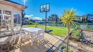 Un patio con una mesa y sillas, un aro de baloncesto y vista a un lago con edificios al fondo.