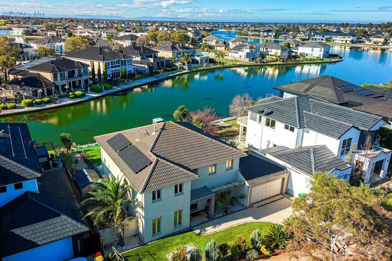 Een woongebied met huizen langs een waterkant, zonnepanelen op daken en een helder uitzicht op het water.