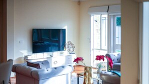 A living room with a flat-screen TV, white furniture, a decorative vase, and a view through large windows. - StayAU Spacious Home w/ Backyard Point Cook (Point Cook)