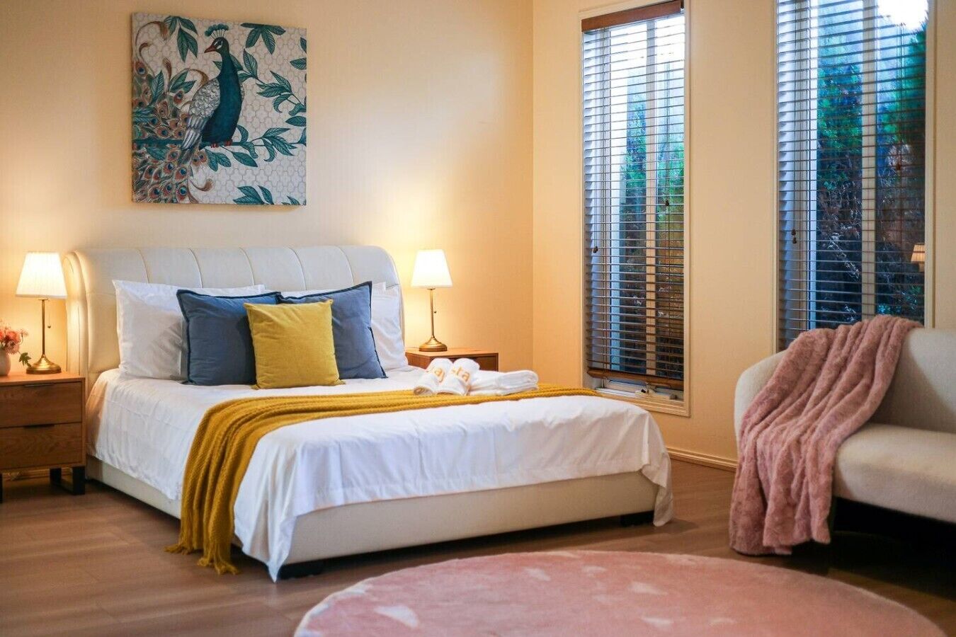 Une chambre à coucher avec un lit, deux tables de chevet, une commode, une chaise, une fenêtre avec des stores et un tableau au mur.