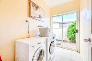 A laundry area with a washing machine and dryer, a bucket on the dryer, and a door leading to a covered outdoor area. - StayAU Spacious Home w/ Backyard Point Cook (Point Cook)