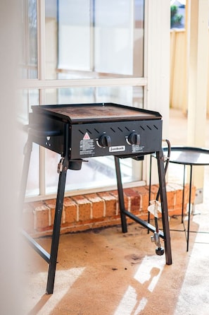 A portable barbecue grill with a control panel, standing on a concrete floor near a window. - StayAU Spacious Home w/ Backyard Point Cook (Point Cook)