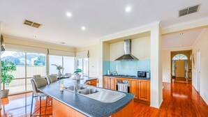 A modern kitchen with a central island, wooden cabinets, and a large window. - StayAU Spacious Home w/ Backyard Point Cook (Point Cook)
