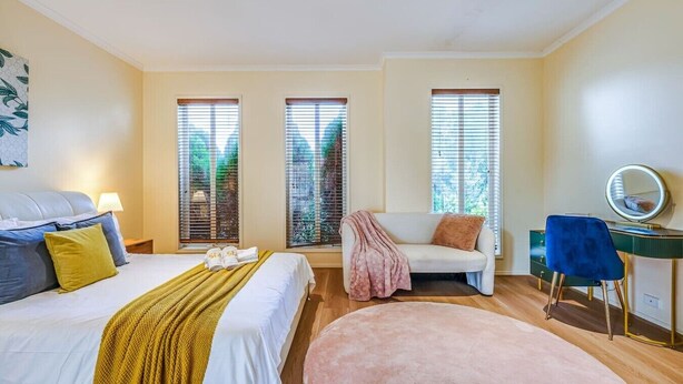 A bedroom with a bed, bedside table, dresser, chair, and a round mirror. - StayAU Spacious Home w/ Backyard Point Cook (Point Cook)