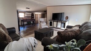 Una sala de estar con un sofá, una mesa de centro y un televisor. Se observa una cocina al fondo.