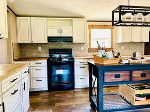 A kitchen with white cabinets, a black stove, and a wooden island with a sink.