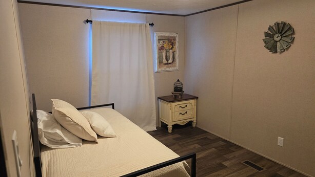 Un dormitorio con cama, mesita de noche, reloj de pared y ventana con cortinas.