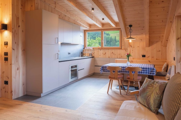 A compact kitchen with modern appliances, a dining area with a table and chairs, and a window with a view of greenery.