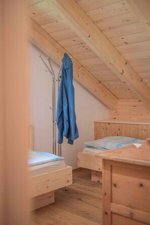 A small, cozy room with two wooden bunk beds, a metal drying rack, and a wooden ceiling.