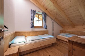 A small, cozy room with a sloped ceiling and wooden walls. There are two wooden beds with matching headboards and a window with curtains.