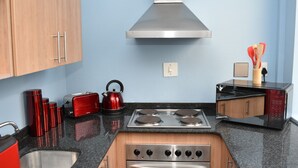 Cocina compacta con estufa de acero inoxidable, hervidor rojo y microondas.