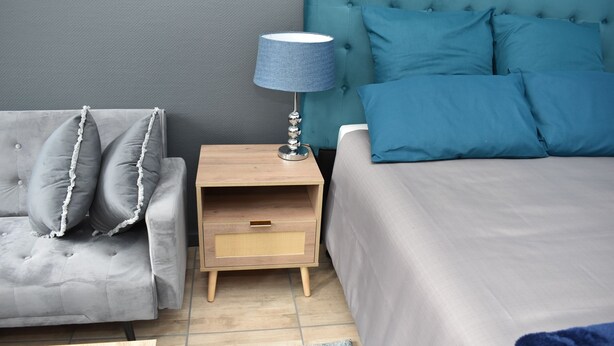 Un dormitorio con un sofá gris, una mesita de noche con lámpara y una cama con ropa de cama azul.
