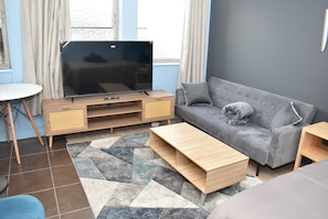 Un salon moderne avec un téléviseur à écran plat, un canapé gris, une table basse en bois et un tapis à motifs.