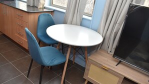 Una cocina compacta con comedor, que incluye una mesa blanca, sillas azules y un televisor.