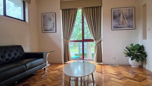 Un salon avec un canapé noir, une table basse ronde et une grande fenêtre avec des rideaux.