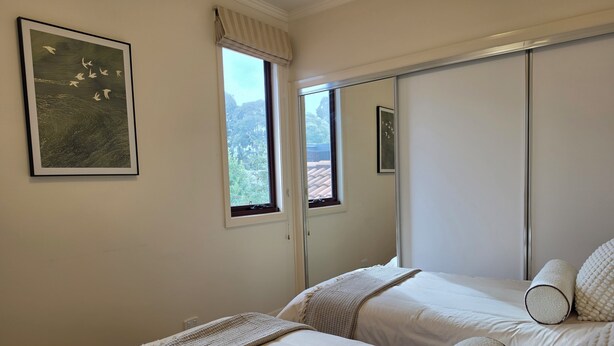 Une chambre avec deux lits, une fenêtre donnant sur les arbres et un miroir au mur.