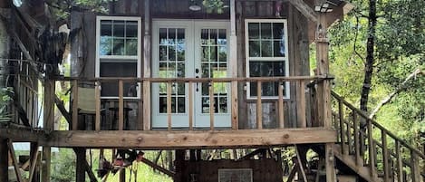 A wooden cabin with a covered deck, a staircase, and a small outdoor seating area.