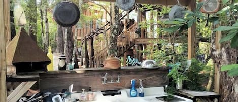 An outdoor kitchen with a wooden structure, hanging pots, and a sink.